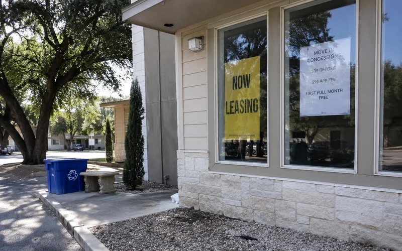 Leasing office window with a now-leasing banner and a concession flyer taped inside the glass