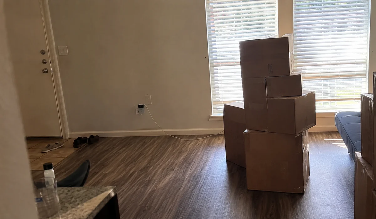 Cardboard moving boxes stacked in an empty Fort Worth apartment with vinyl plank flooring after a lease break