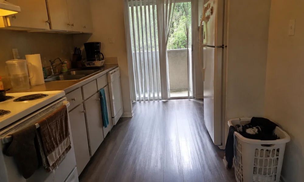 Galley kitchen in a Tarrant County apartment with laminate countertops, white appliances, and vinyl plank flooring