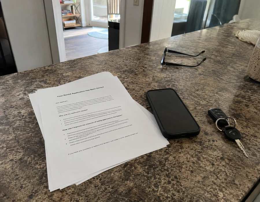 Rental application denial letter on a Fort Worth apartment kitchen counter in harsh midday light