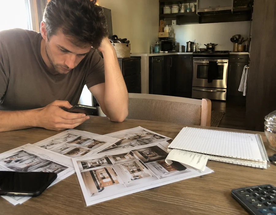 Renter at a kitchen table with a phone and printed apartment listings