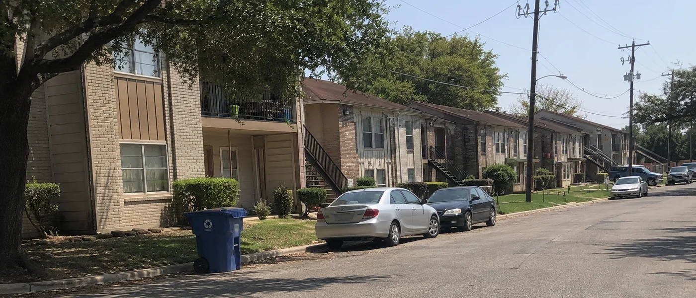 Row of Tarrant County apartment buildings along a residential street with parked cars and live oaks