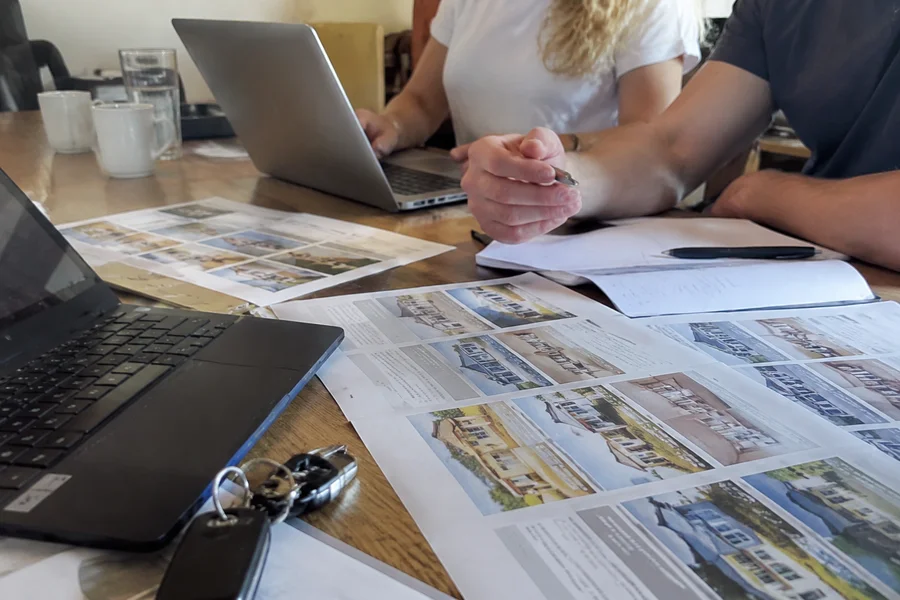 Two laptops and printed property criteria sheets on a shared desk