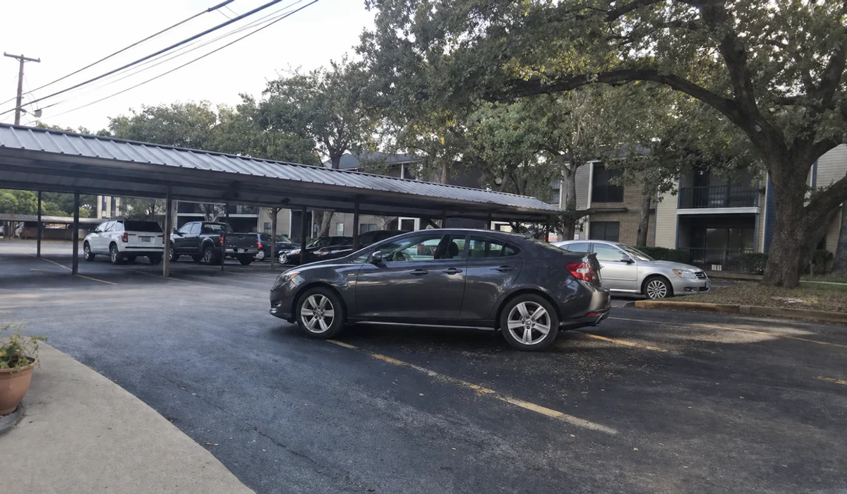 Fort Worth apartment complex near Loop 820 with metal-roof carports and live oaks under a grey sky
